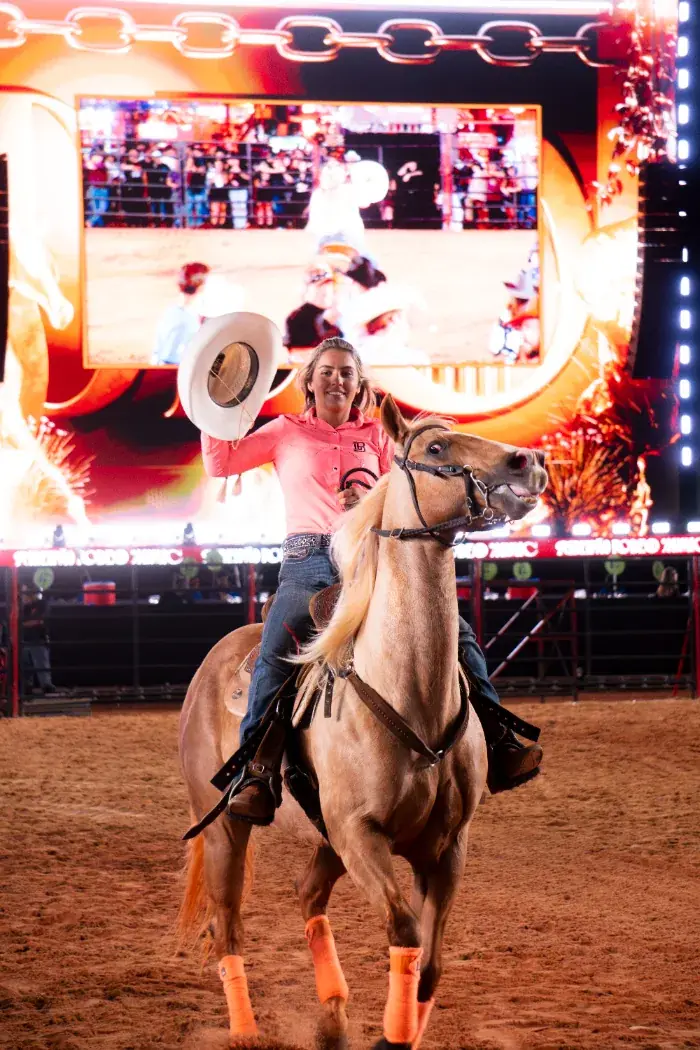 Amazona em cavalo palomino saudando a plateia na arena de rodeio