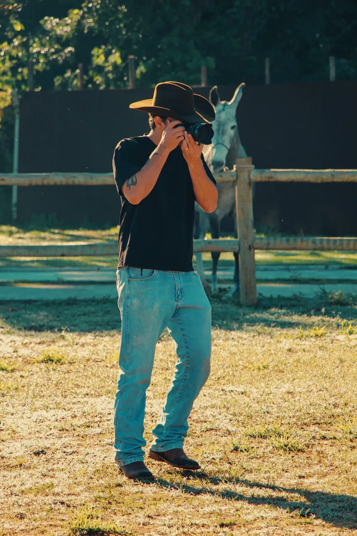 Fotógrafo com chapéu registrando cavalo no curral